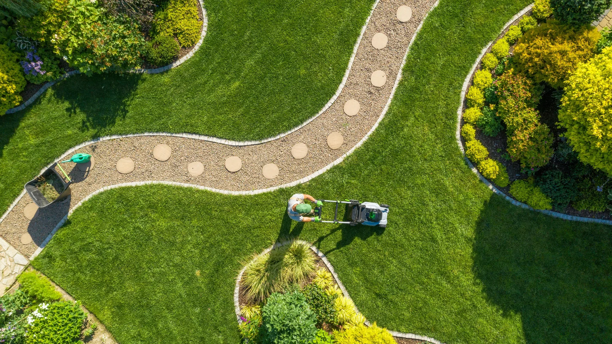 A directly overhead drone shot shows a landscaped backyard with a curving stone-and-gravel stepping-stone path cutting throug